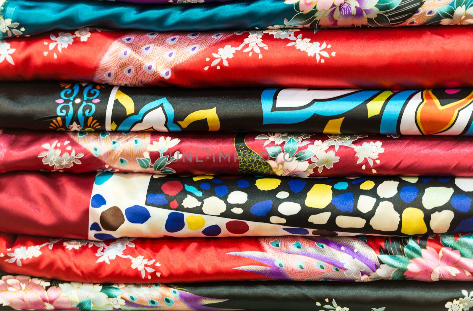 Pile of vibrant folded clothes. Variations of silk dresses with traditional asian design. Beautiful red, black and blue fabrics with abstract ornate pattern. Stack of bright textured materials.