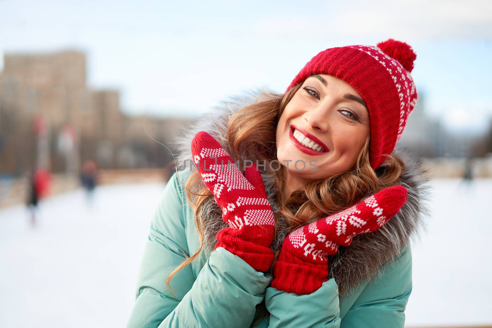 Beautiful lovely middle-aged girl curly hair warm winter jackets red knitted hat glove stands ice rink background Town Square Christmas mood lifestyle Happy holiday woman snowy day Winter leisure