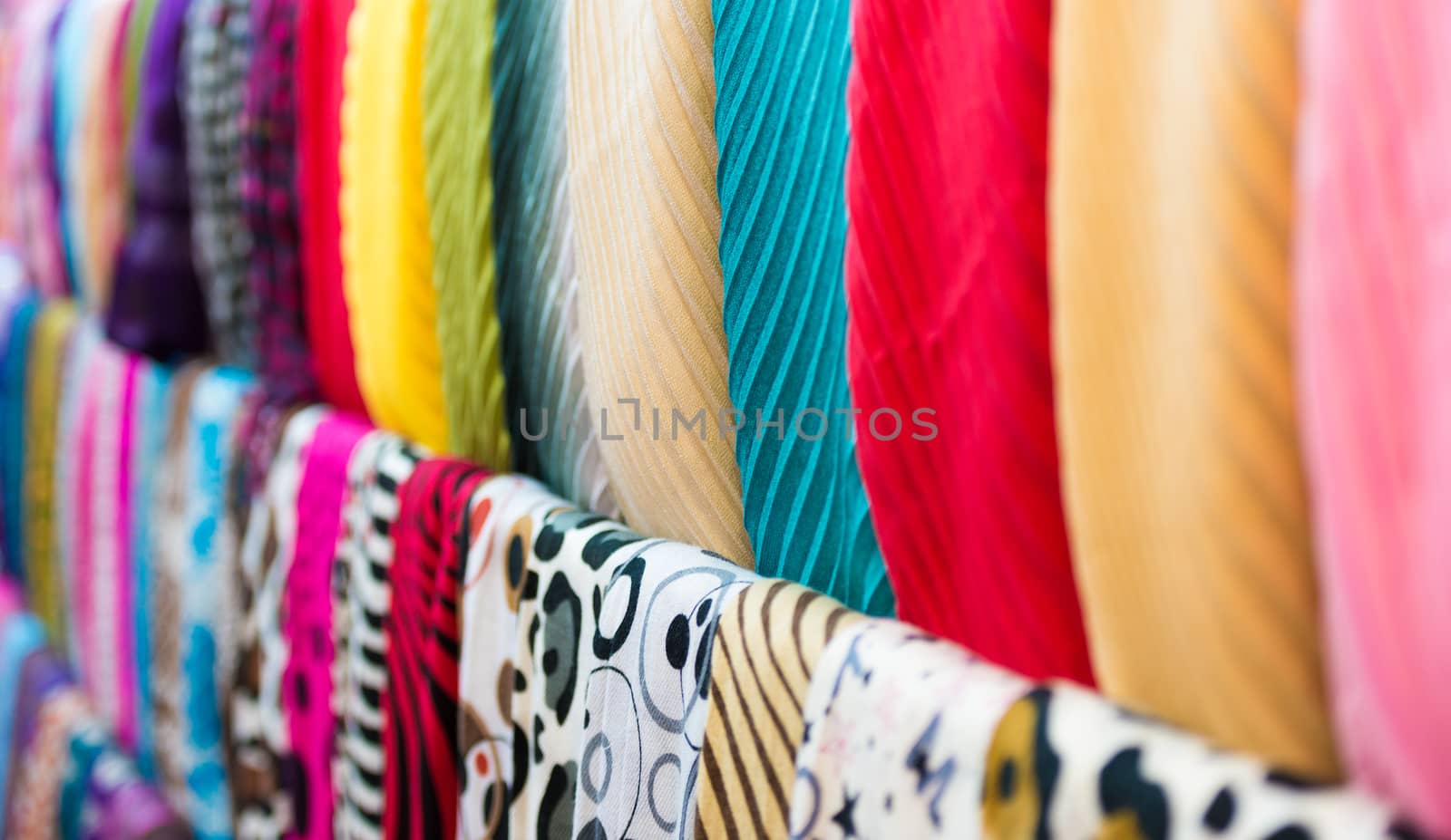 Close up view of colorful row of new scarves ready for sale at shop. Focus on blue and red ones. Going shopping and retail of casual clothes. Textiles and materials for sale. Trade and commerce.