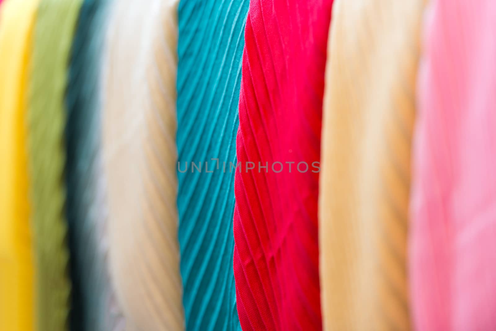 Close up view of colorful row of new scarves ready for sale at shop. Focus on blue and red ones. Going shopping and retail of casual clothes. Textiles and materials for sale. Trade and commerce.