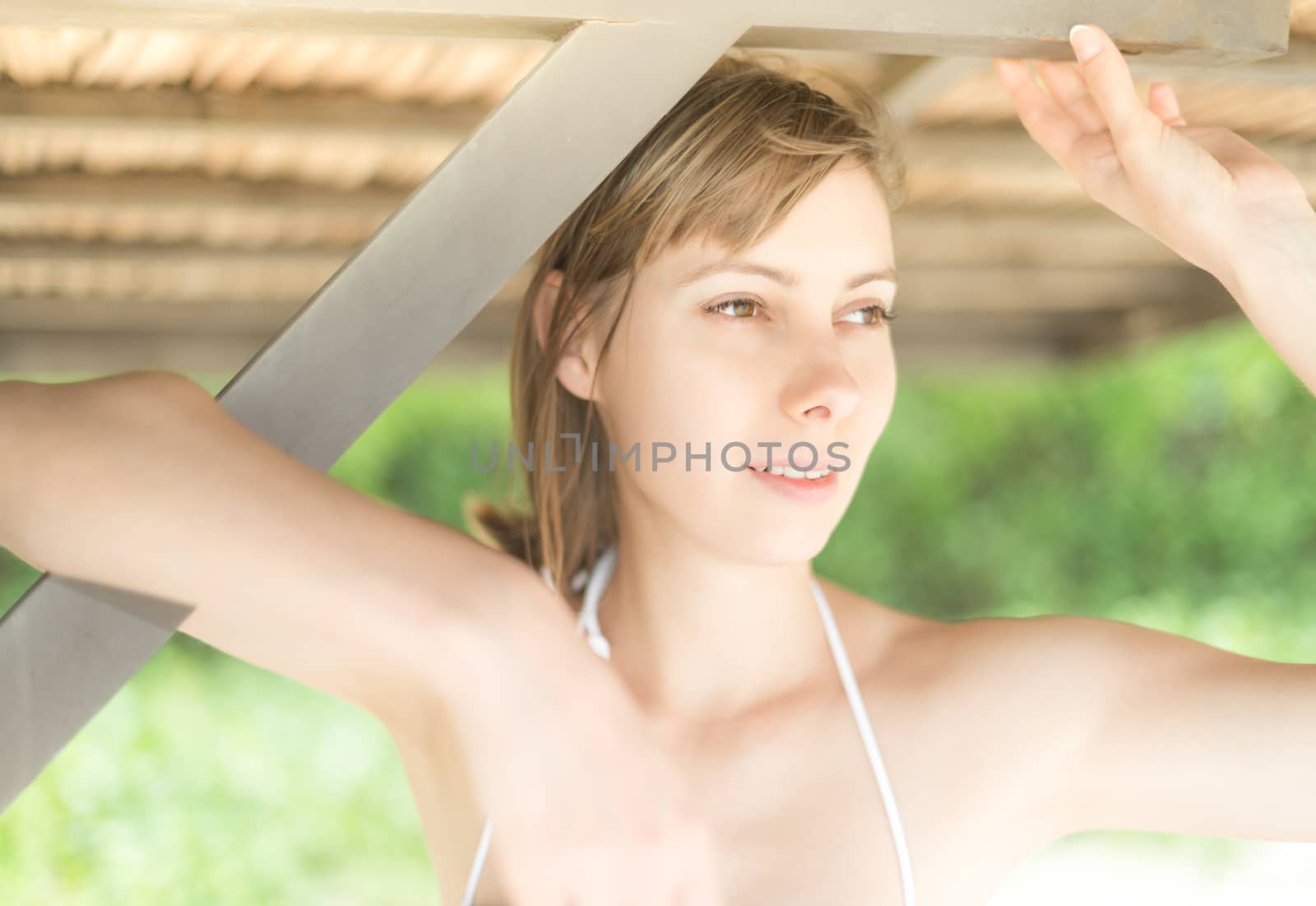 Pretty girl standing under wooden pier and smiling. Beautiful young woman on beach. Green trees in background. Leisure activity outdoor. Idea of summer vacation. Popular tourist place for holiday.