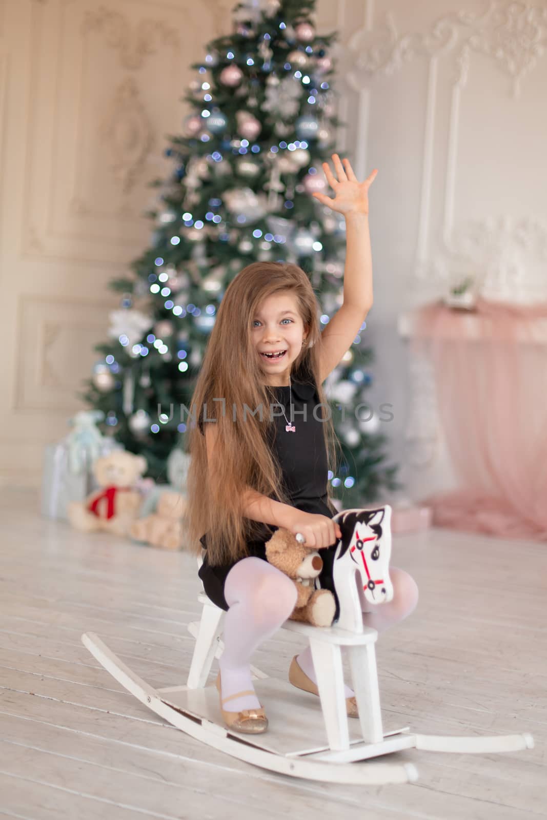 Beautiful little girl rejoices at the wooden rocking horse, a Christmas present from Santa.