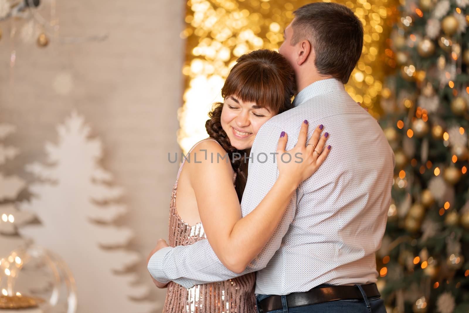 A joyful girl hugs a guy among sparkles and gerlands at a Christmas party.