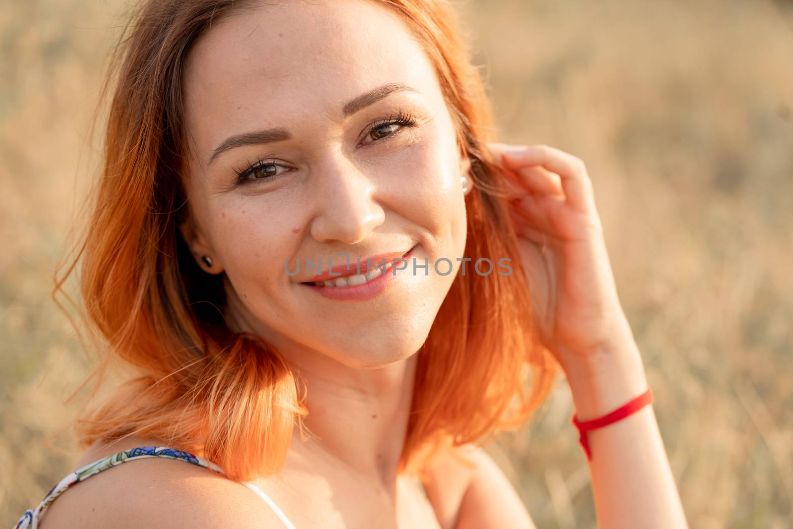 Tender beautiful red-haired girl enjoys the sunset in a field with a hill