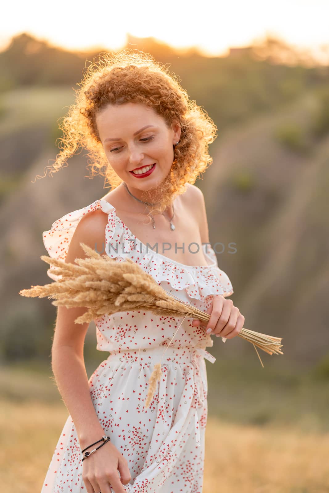 Beautiful tender girl in a white sundress walks at sunset in a field with a spikelet bouquet. by Try_my_best