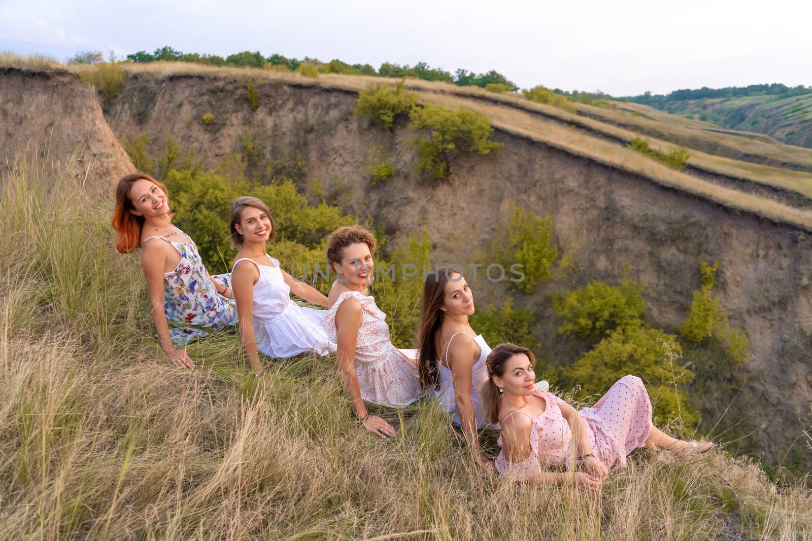 A cheerful company of beautiful girls friends enjoy a picturesque panorama of the green hills at sunset.