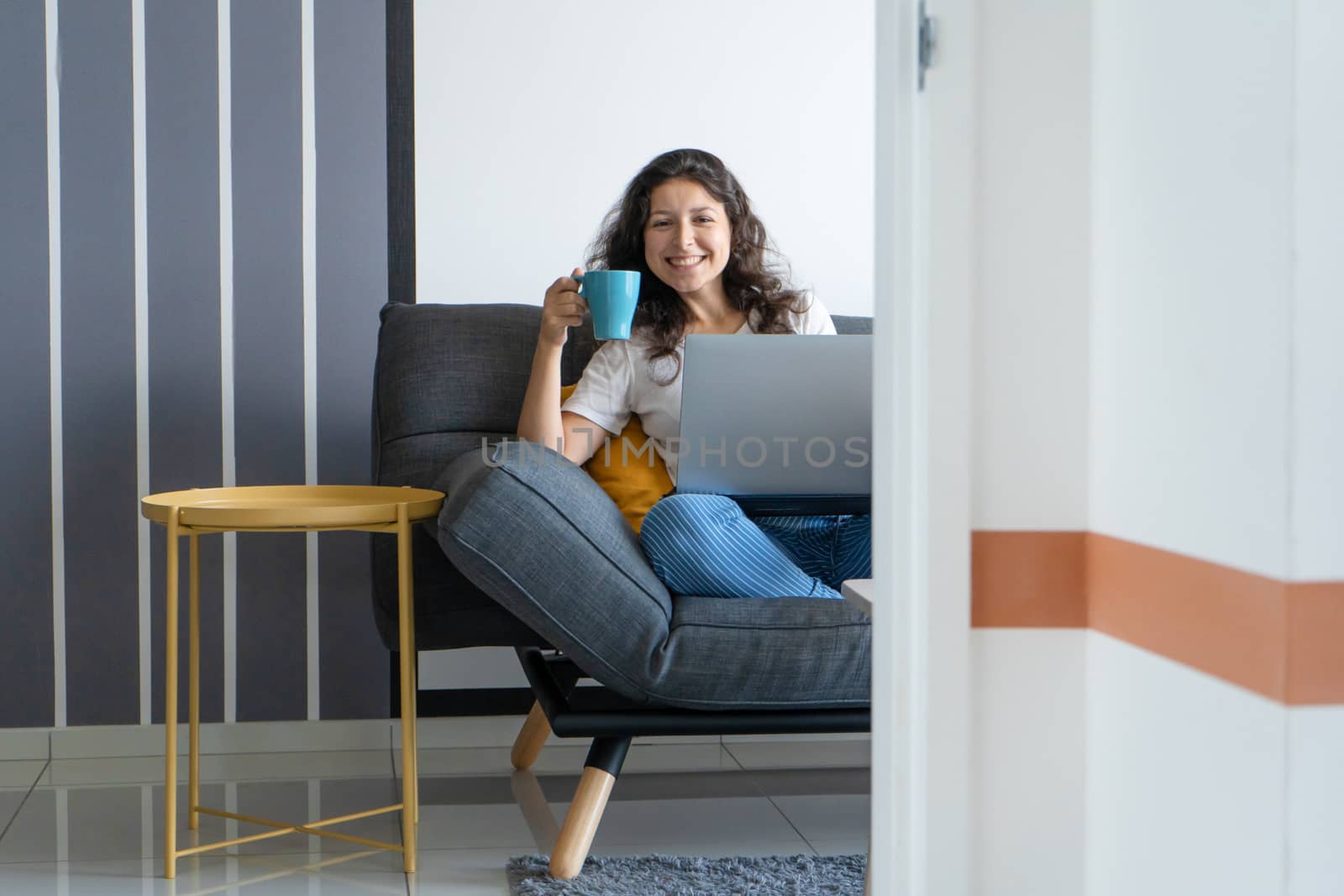 Beautiful girl sitting with a laptop on a sofa in a stylish room. Work from home. Work atmosphere in a good mood.