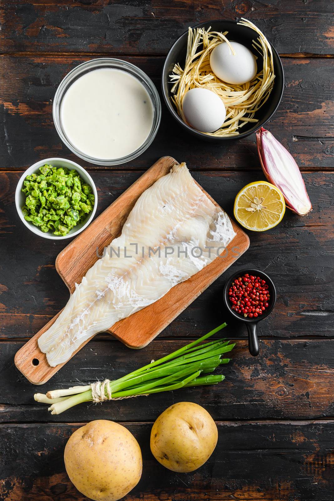 Raw organic Cod fillet fish and chips ingredients beer batter, potatoe, tartar sauce, minty mushy peas, lemon , shallot, mint, garlic, salt, peppercorns on rustic old wood table top view vertical by Ilianesolenyi