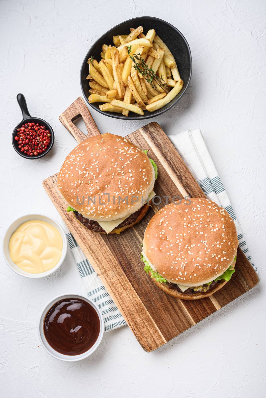 Two ground beef burger and french fries on white textured background.