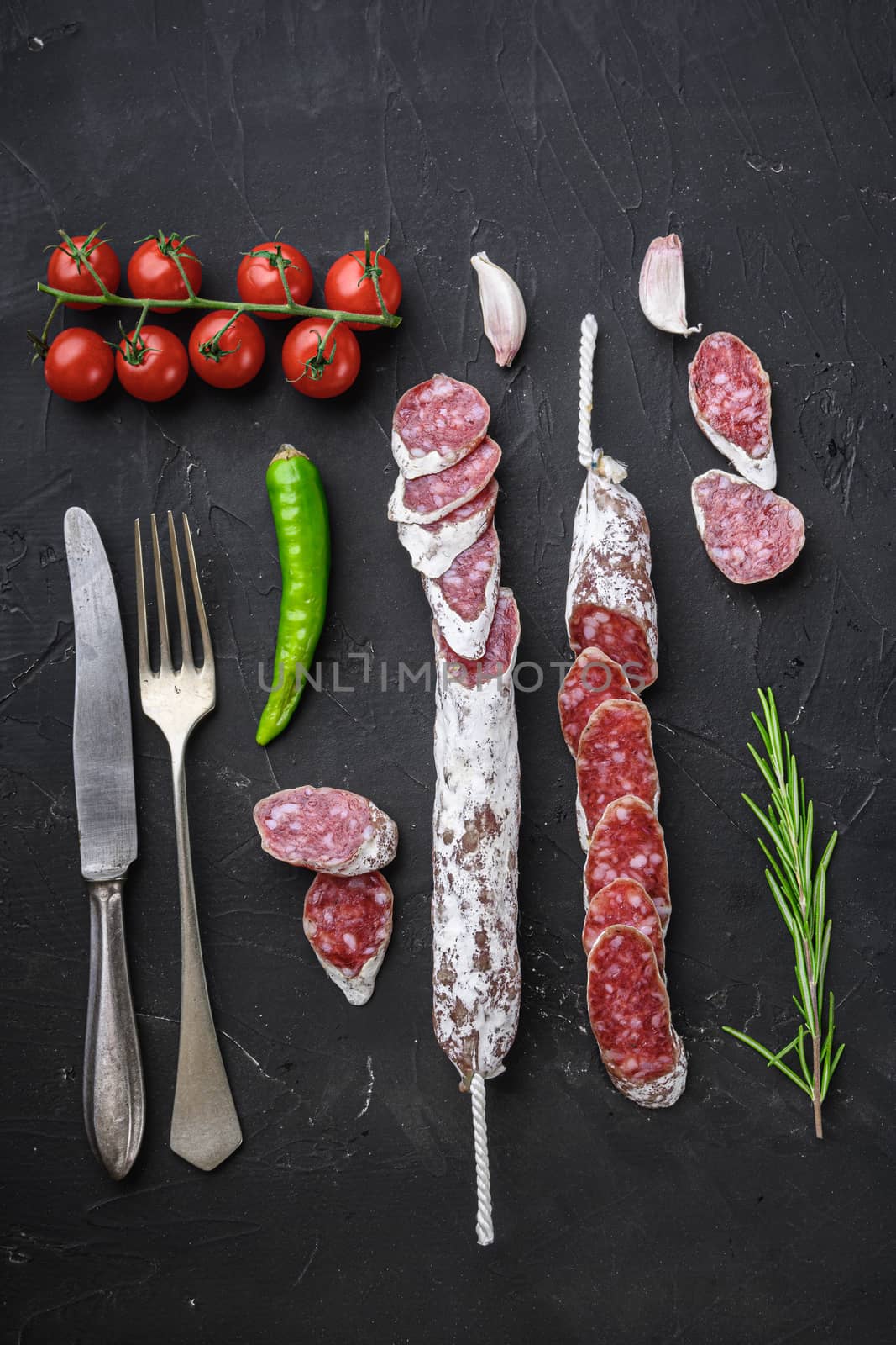 Dry cured fuet salami sausage slices on balck background, top view.