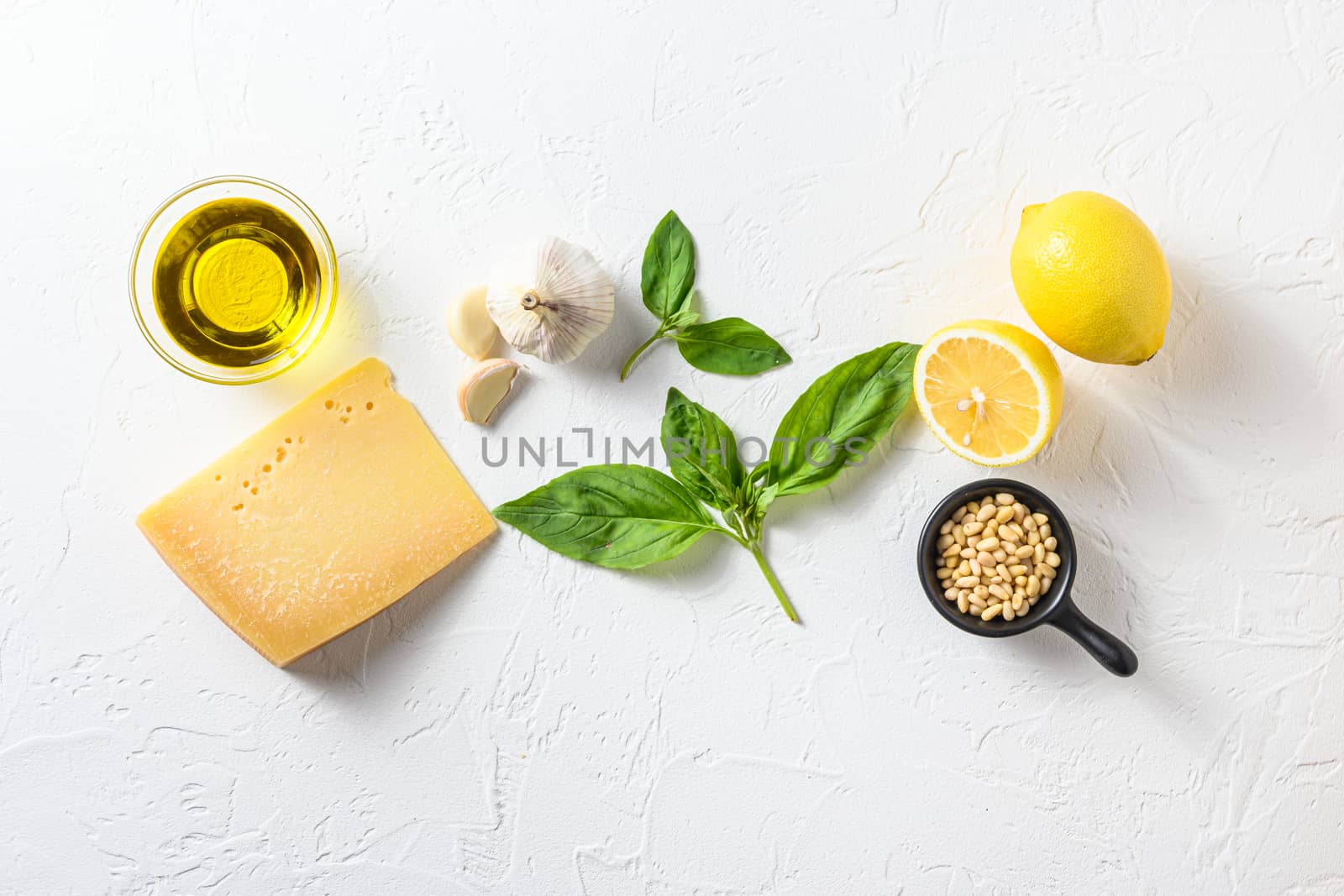 Genovese pesto ingredients concept or ingredients Parmesan cheese, basil leaves, pine nuts, olive oil, garlic, salt, pepper and mortar for cooking on white old stone table top view with copy space.