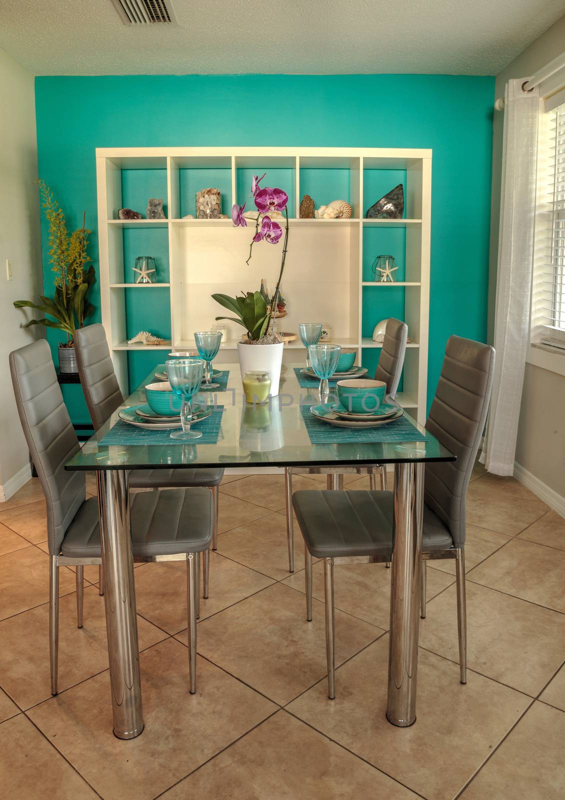 Glass dinner table with aqua blue dishes and a tropical nautical seashell background with a blue wall.