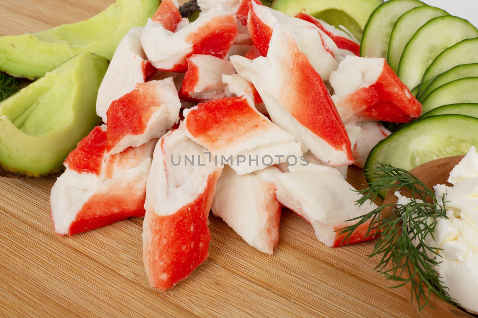 Crab sticks cut meat and vegetables avocado cut cucumbers on wooden cutting board close up