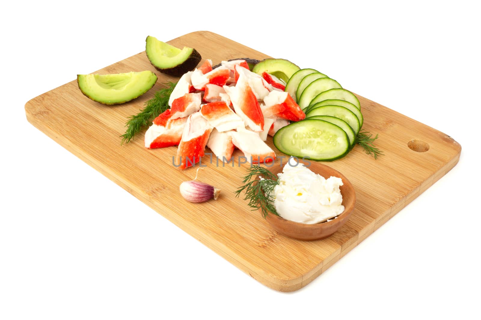 Crab sticks cut meat and vegetables avocado cut cucumbers on wooden cutting board isolated on white background