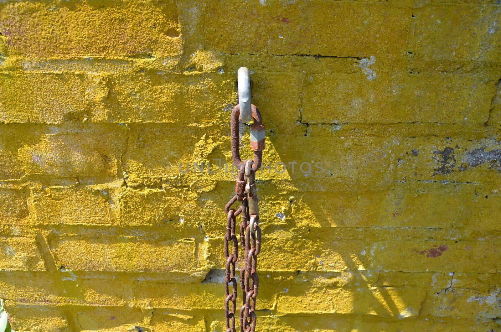 rusty metal chain hanging on yellow and red bricks or masonry