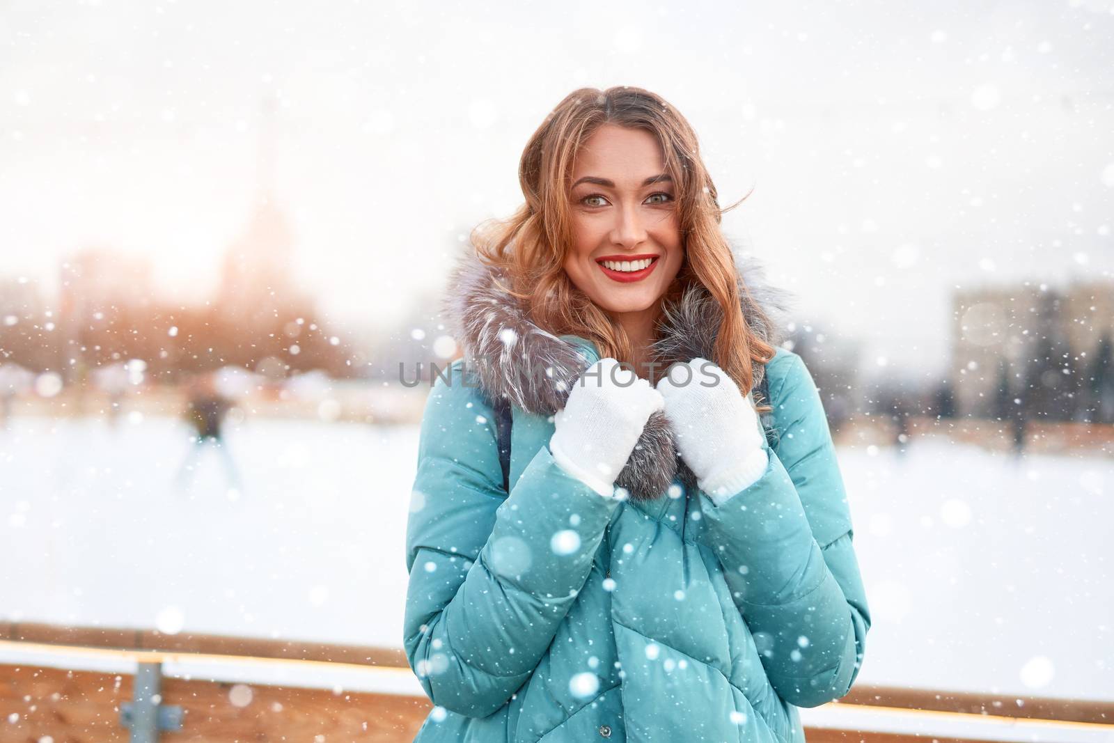Beautiful lovely middle-aged girl curly hair warm winter jackets white glove stands ice rink background Town Square. Christmas mood lifestyle Happy holiday woman walk snowy day Winter leisure