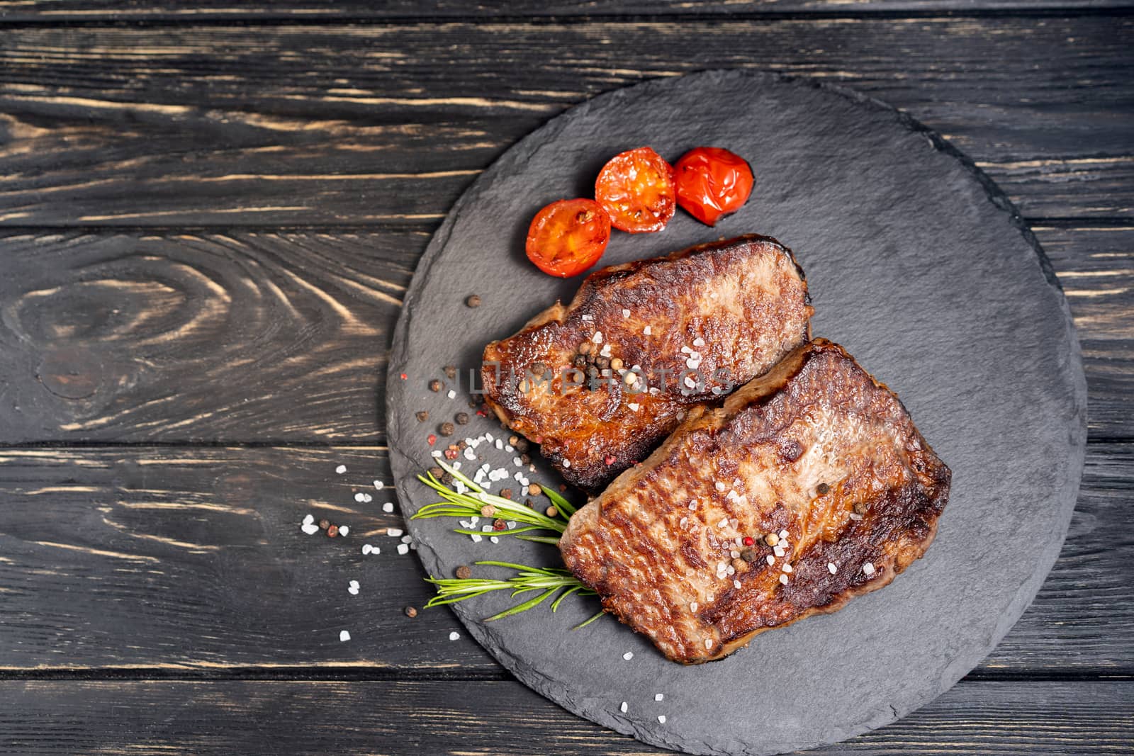 A juicy piece of fried meat with grilled cherry tomatoes lies on a stone plate against a black wooden table. Degree of roasting well done. Food concept with copy space