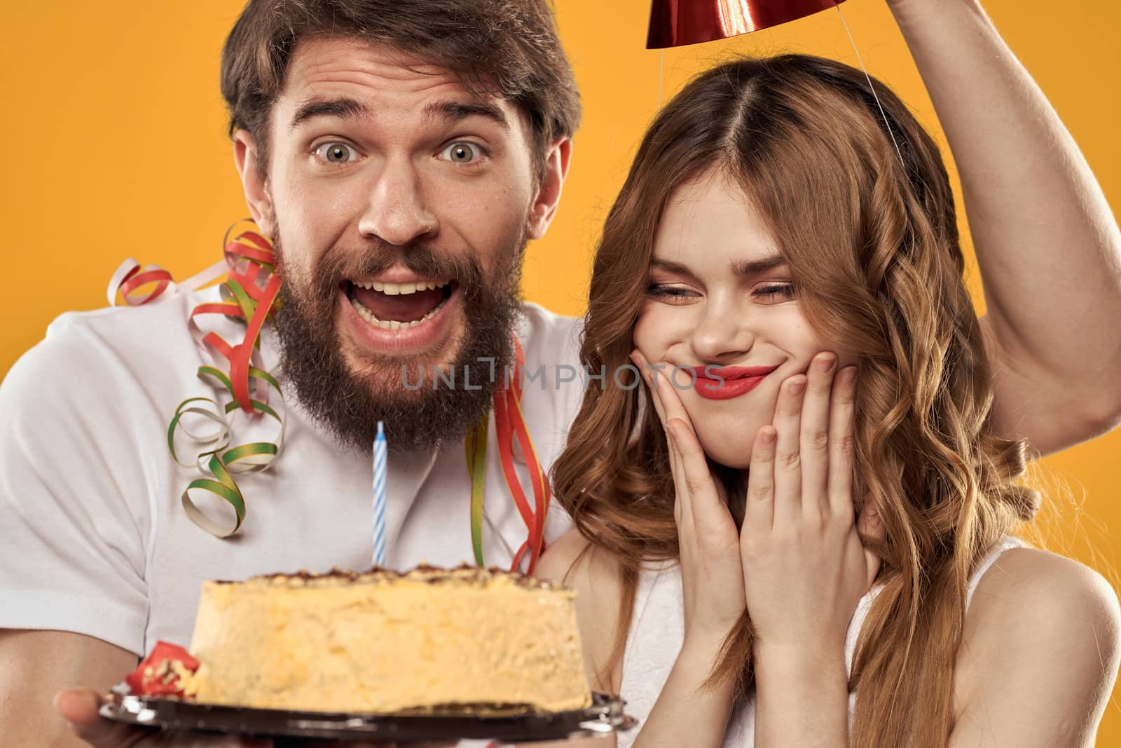 Man and woman birthday festive cake yellow background and caps on the headv. High quality photo