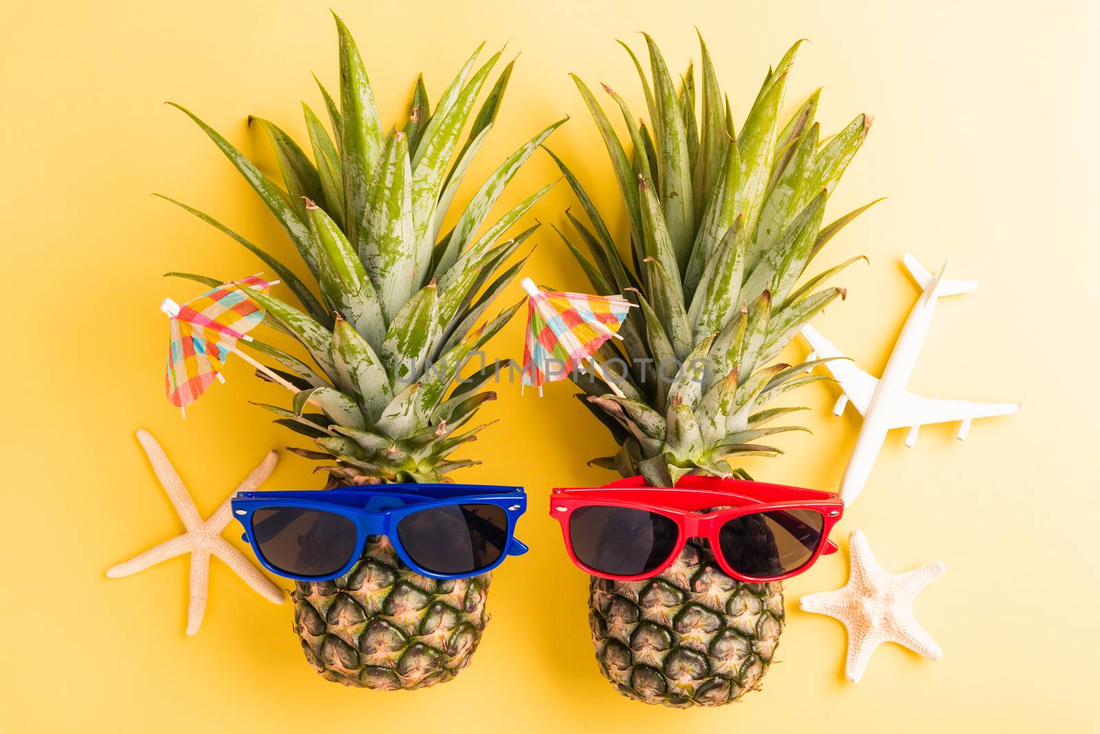 Celebrate Summer Pineapple Day Concept, Top view flat lay of funny two pineapples in sunglasses with model plane and starfish, studio shot isolated on yellow background, Holiday summertime in tropical