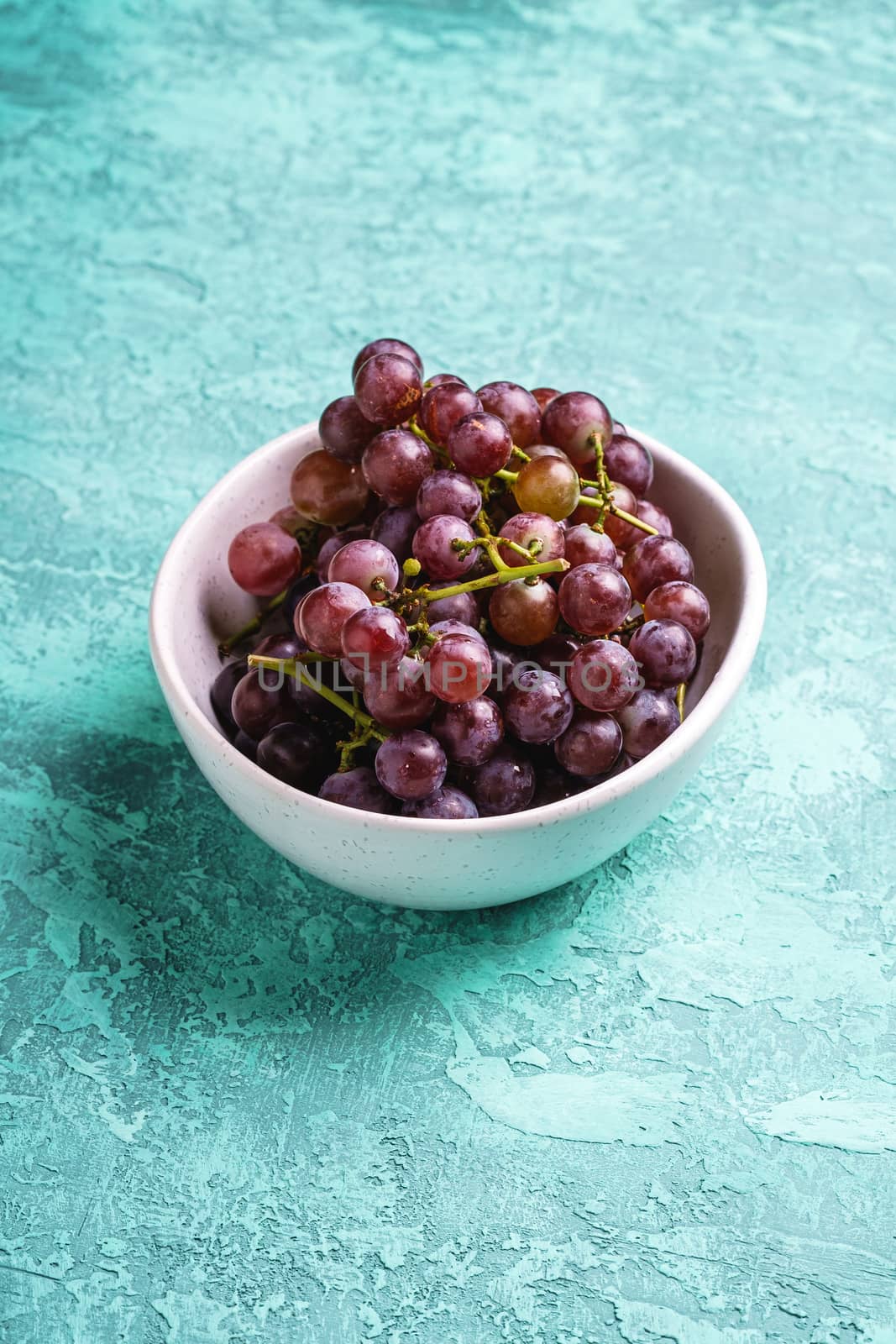 Fresh ripe grape berries in bowl on turquoise textured background, angle view