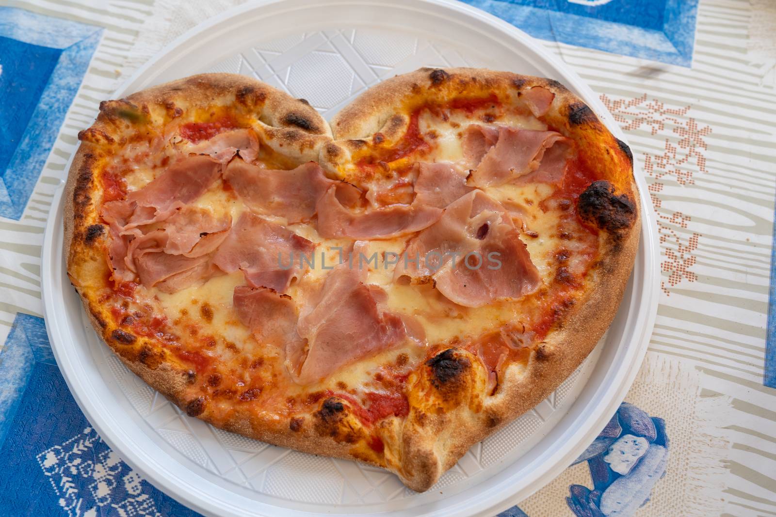 Heart shaped pizza with tomatoes and ham for Valentines Day on white plastic plate on the table,Food concept of romantic love