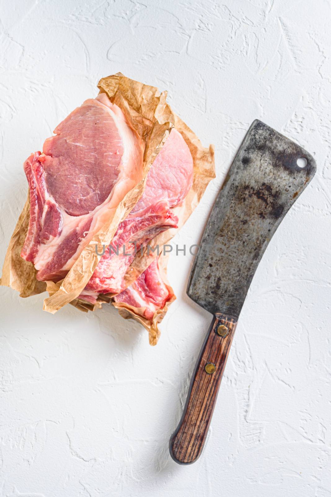 Fresh and raw organic pork loin chops . Top view Vertical. with meat butcher cleaver on white stone background. by Ilianesolenyi