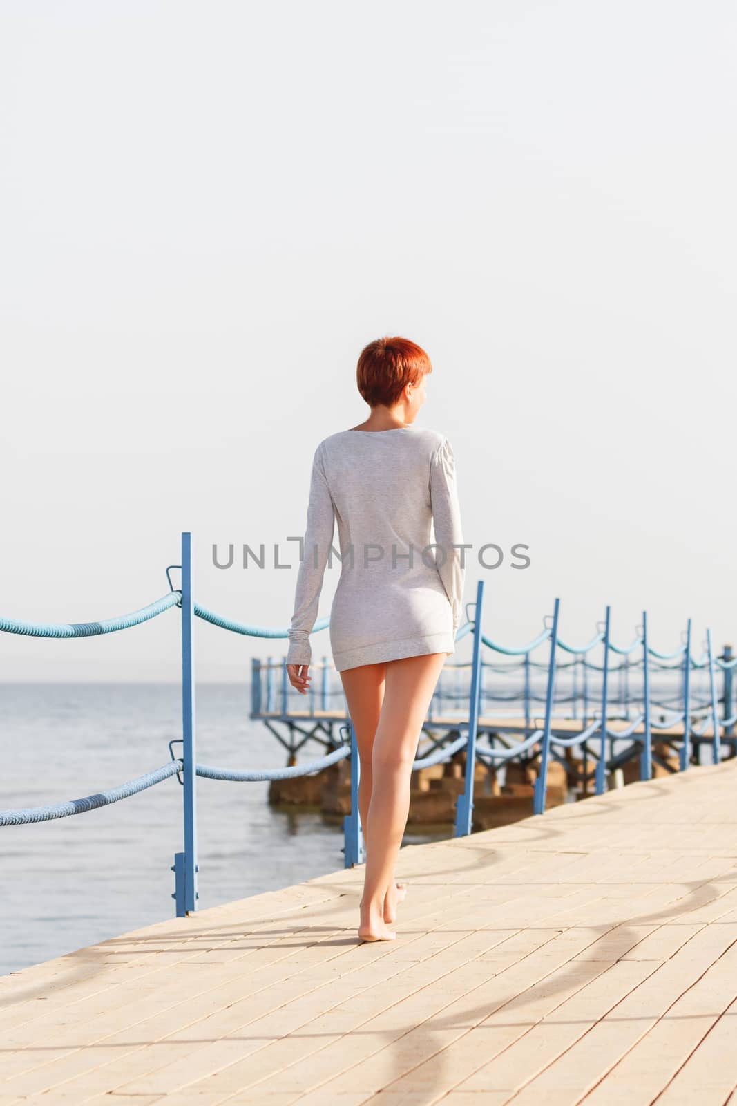 Young woman with red short hair cut on wooden pier. Coastal morning. Natural beauty. Happiness and power of youth.