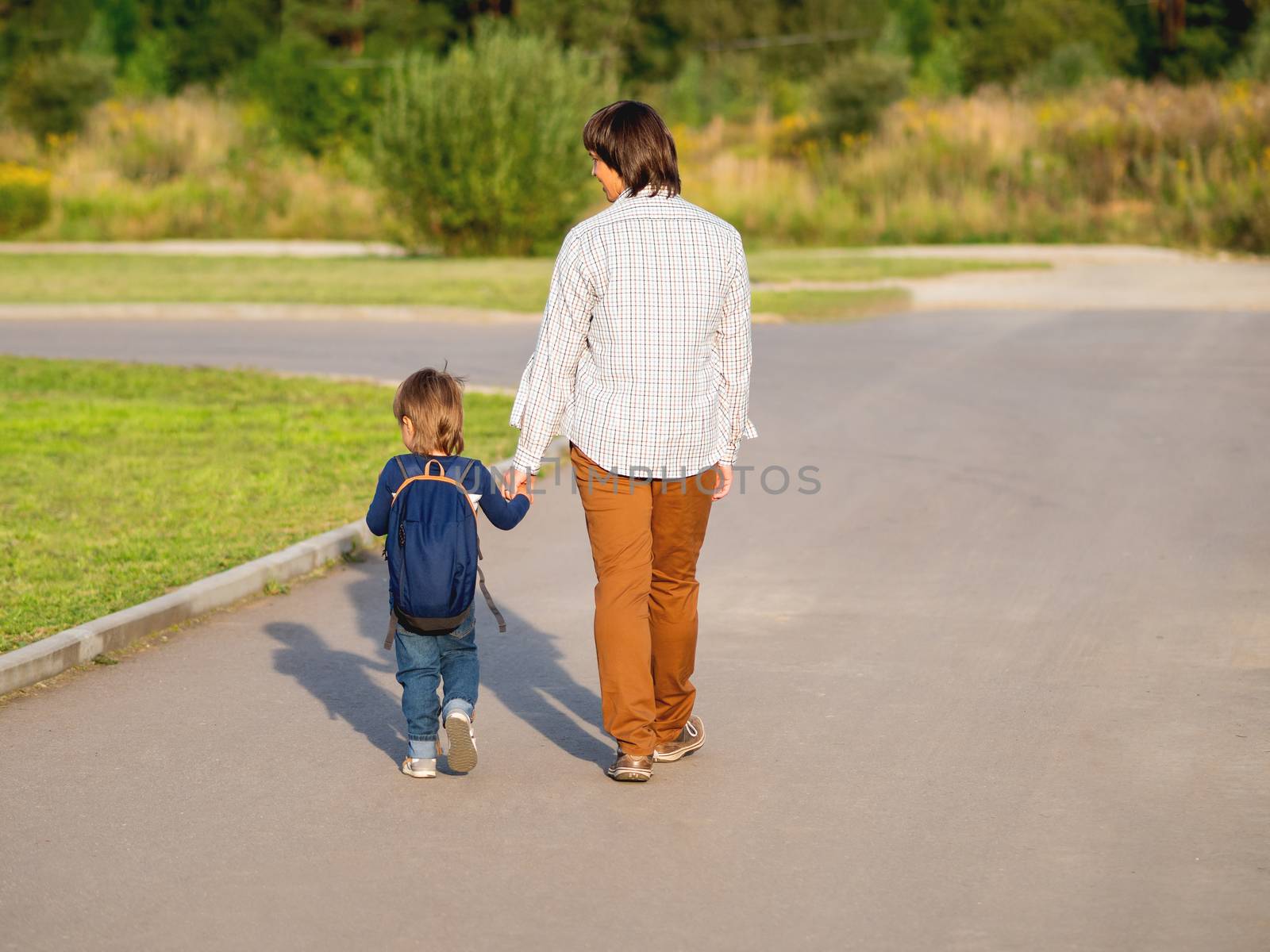 Father takes his son to school. Back to school after summer holidays. Dad and kid walk on street hand in hand. Family time, moral support.