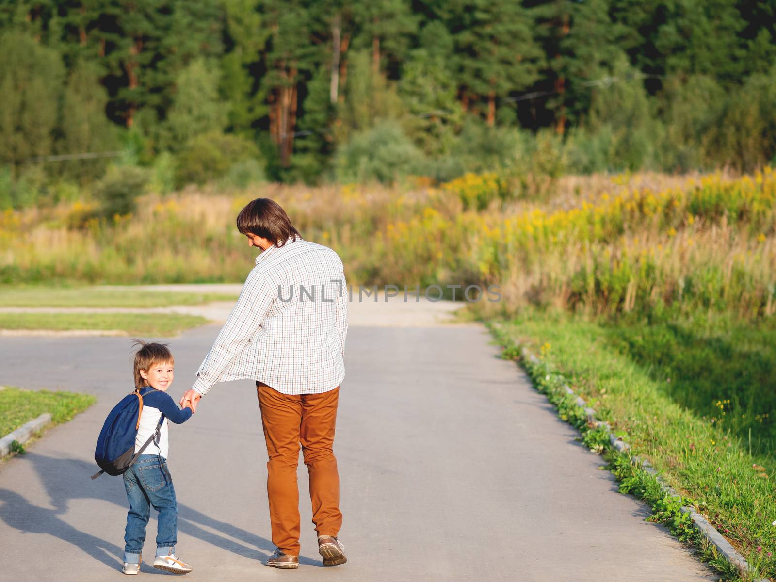 Father takes his son to school. Back to school after summer holidays. Dad and kid walk on street hand in hand. Family time, moral support.