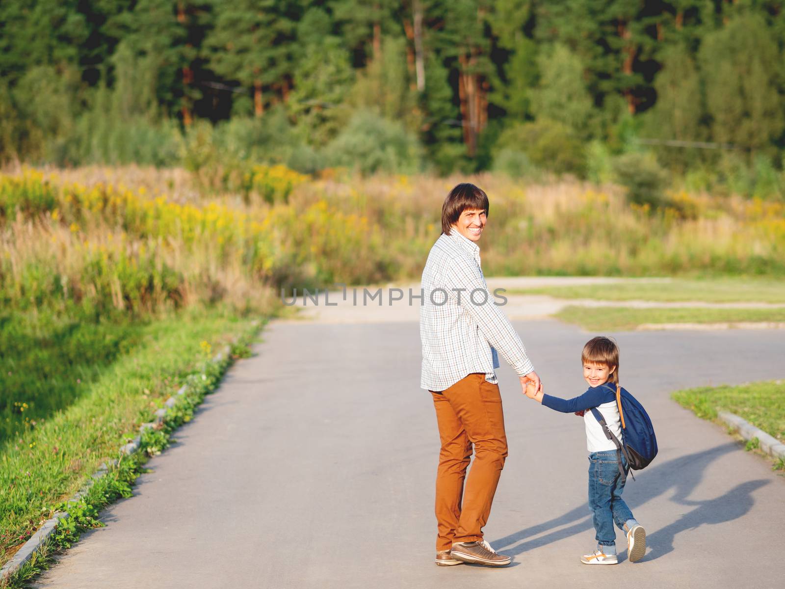 Father takes his son to school. Back to school after summer holidays. Dad and kid walk on street hand in hand. Family time, moral support.