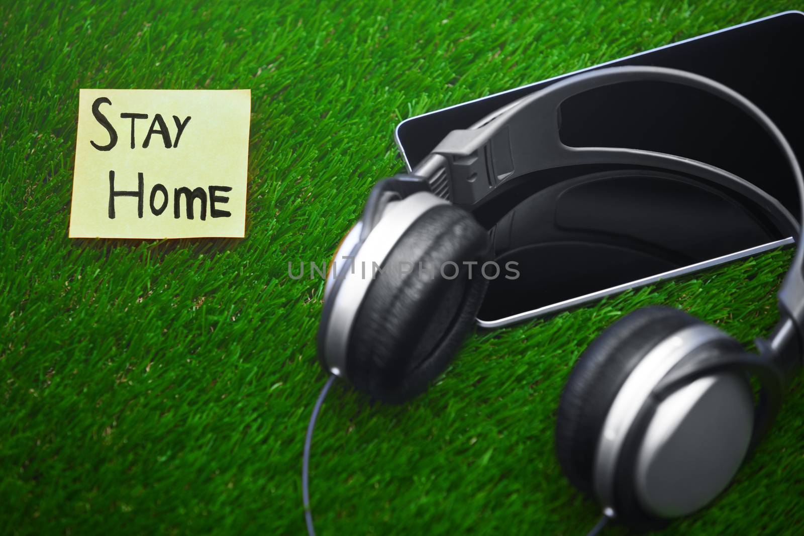 Stay Home text on sticky note on a grass with headphones and dig by Novic