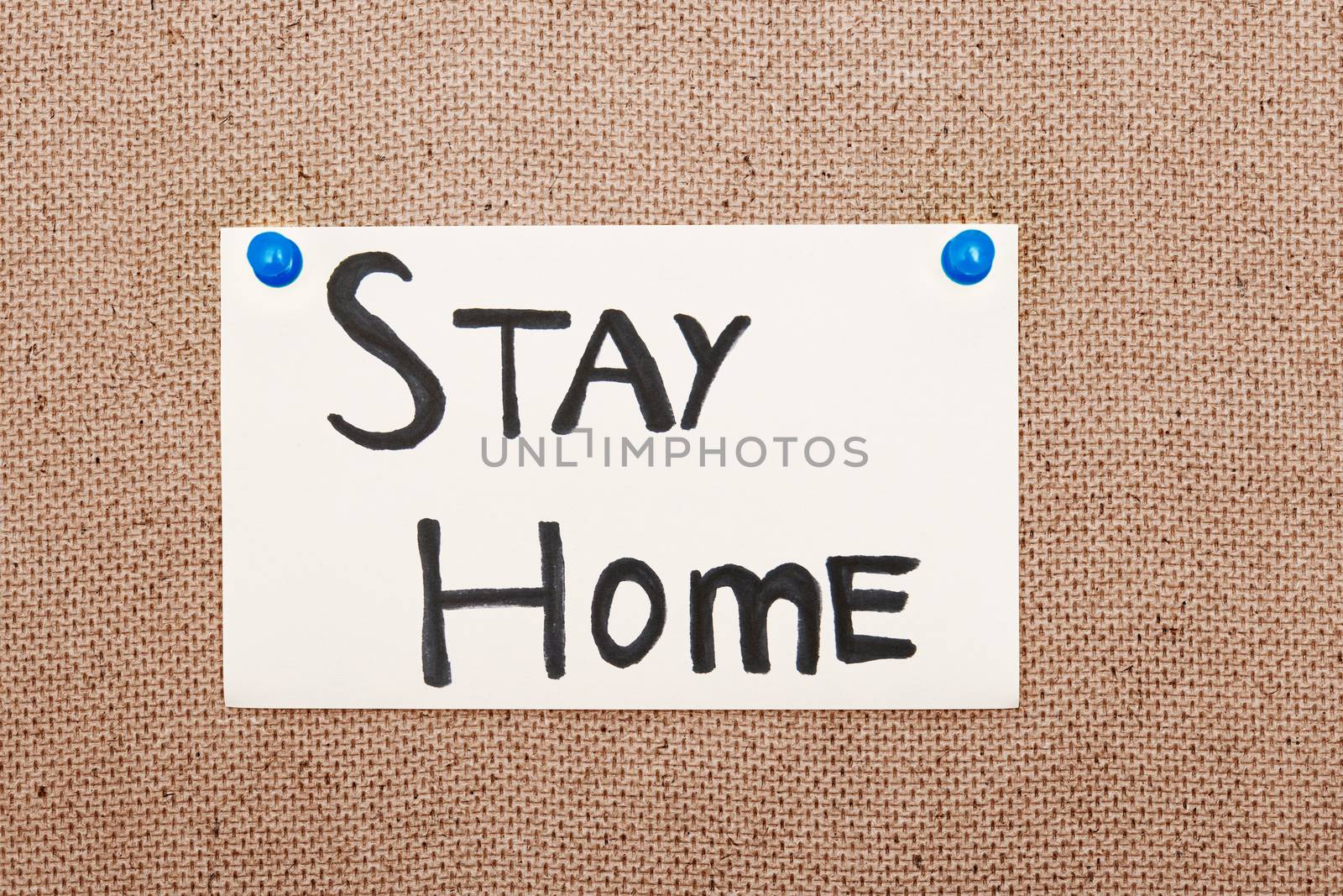 Adhesive note with Stay Home text attached to the bulletin board by pushpins