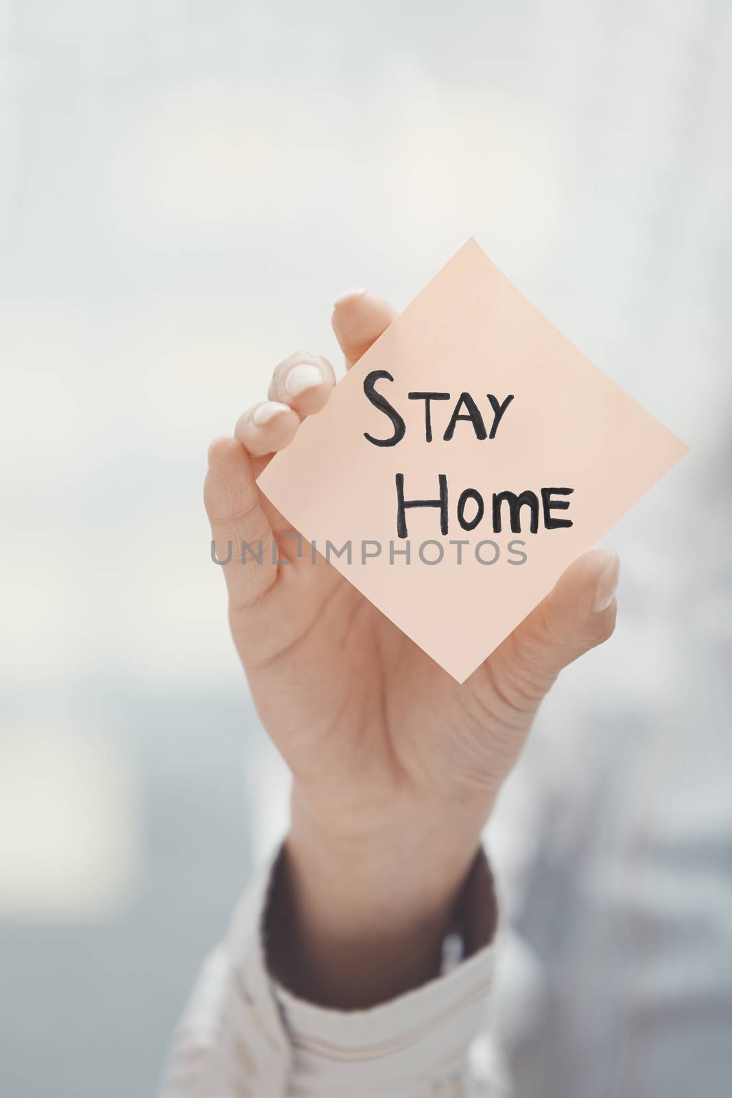 Hand holding sticky note with Stay Home text by Novic