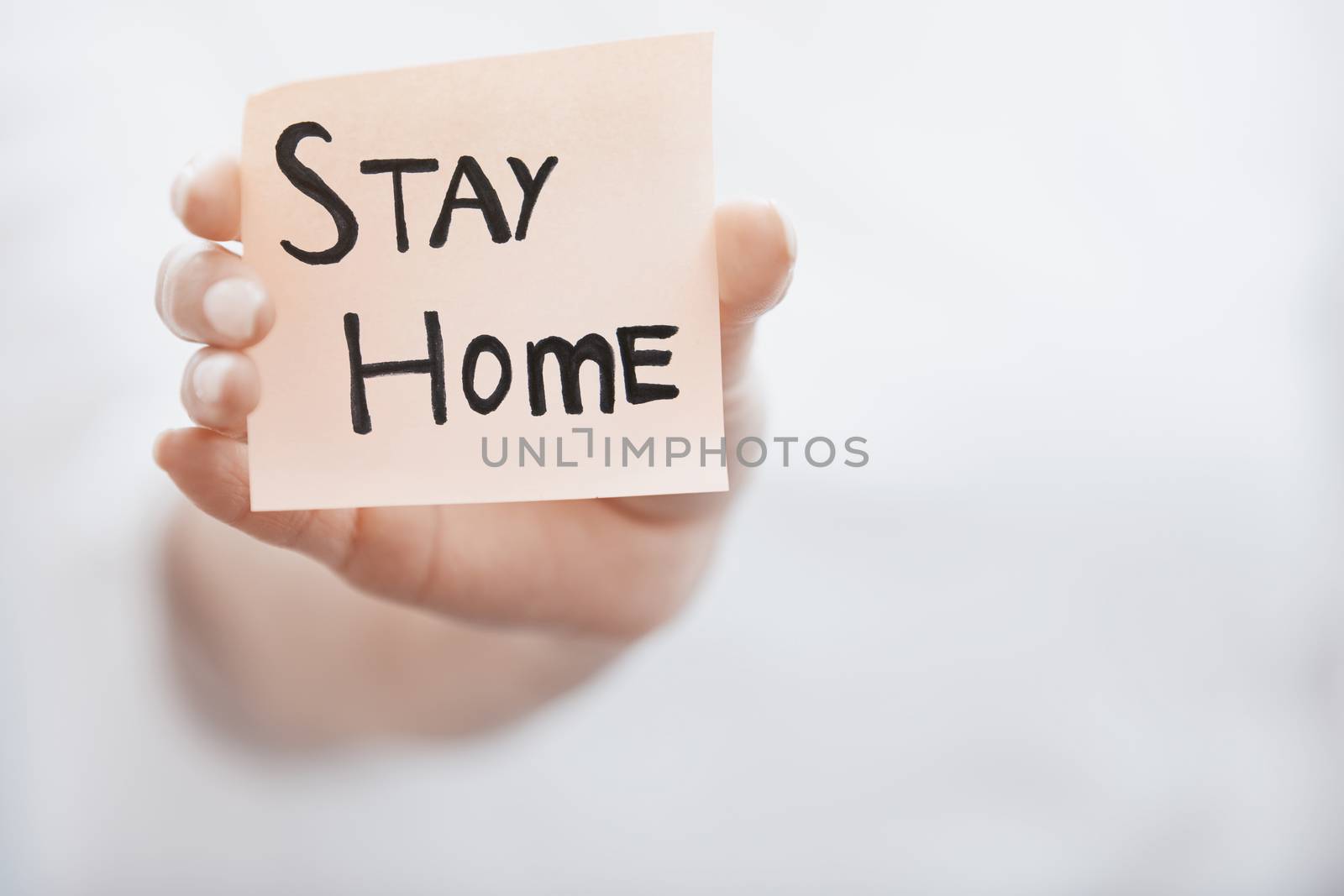 Hand holding sticky note with Stay Home text