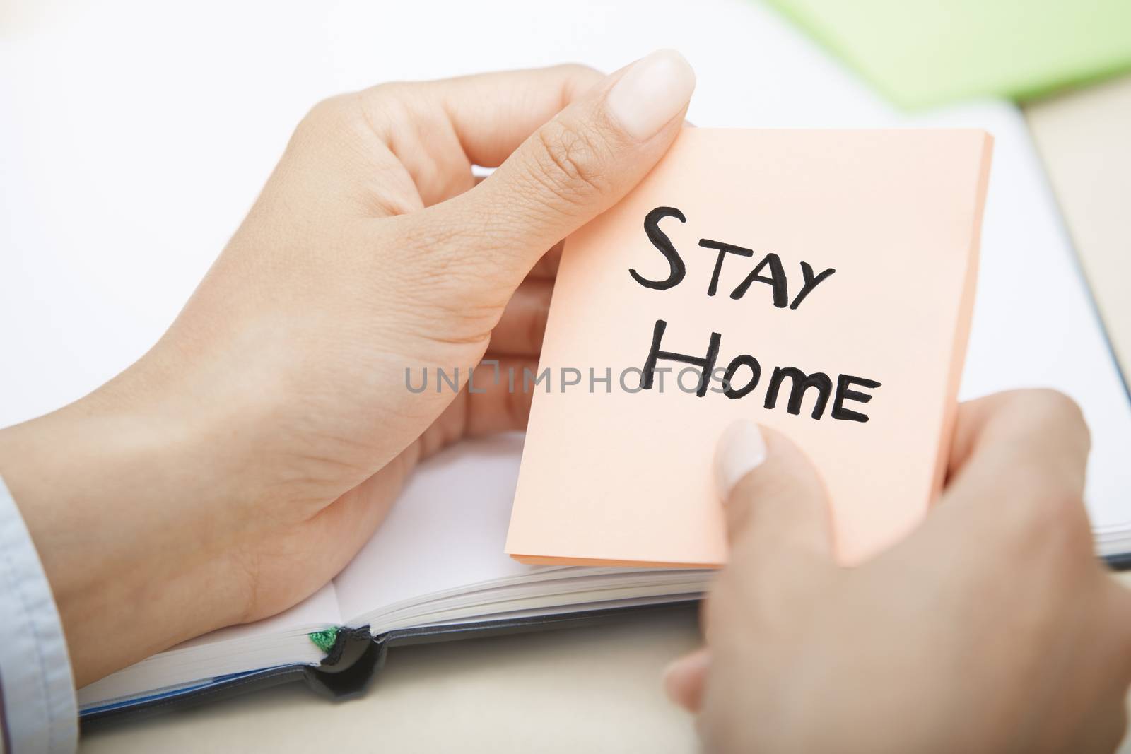 Hands holding pink sticky note with Stay Home text by Novic