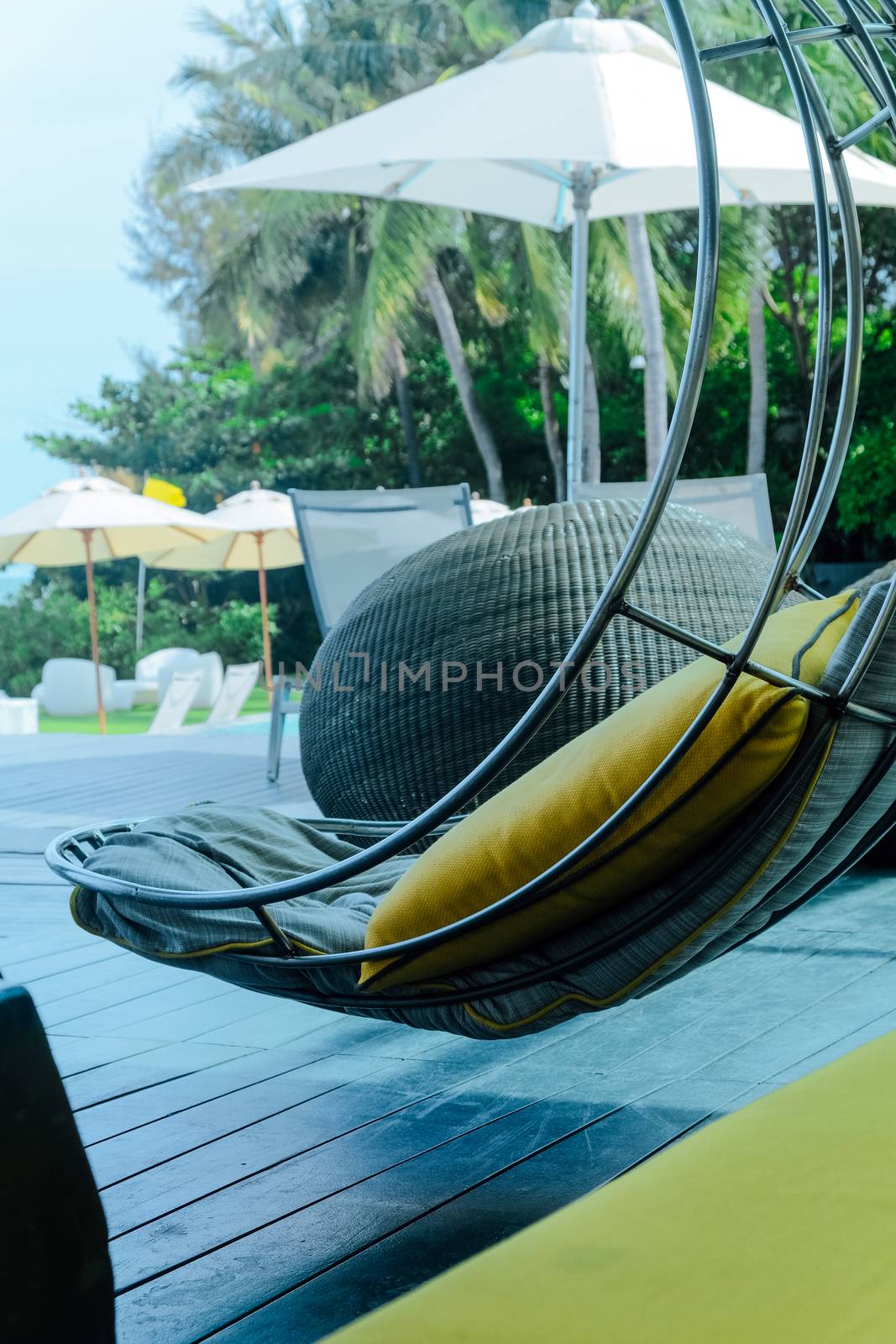 Image of Relaxing chairs with pillows beside swimming pool by ponsulak