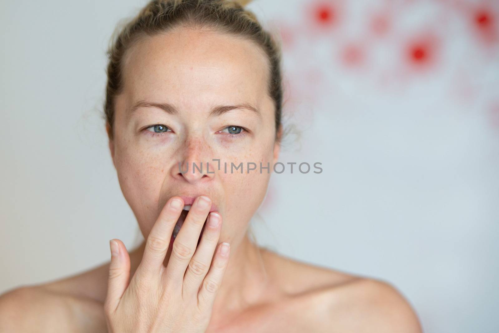 Closeup portrait headshot of sleepy young woman covering her wide open mouth while yawning by her palm. Face expression,emotion, body language concept.