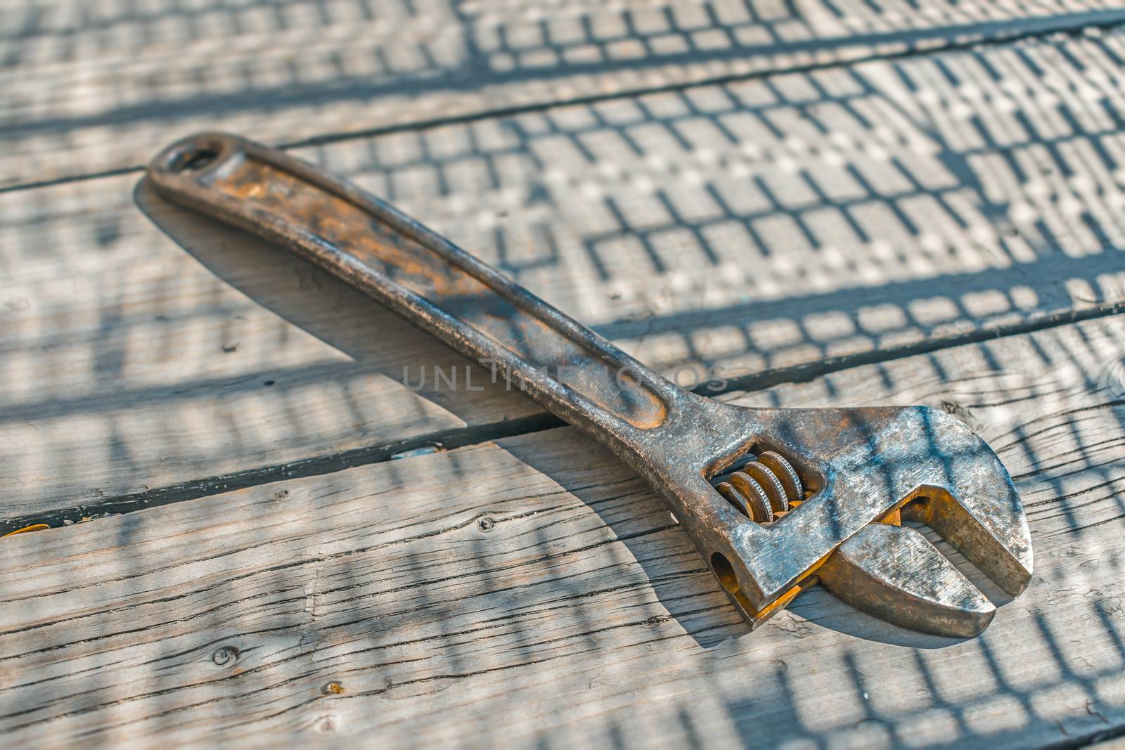A rusty steel adjustable wrench lies on an old wooden floor