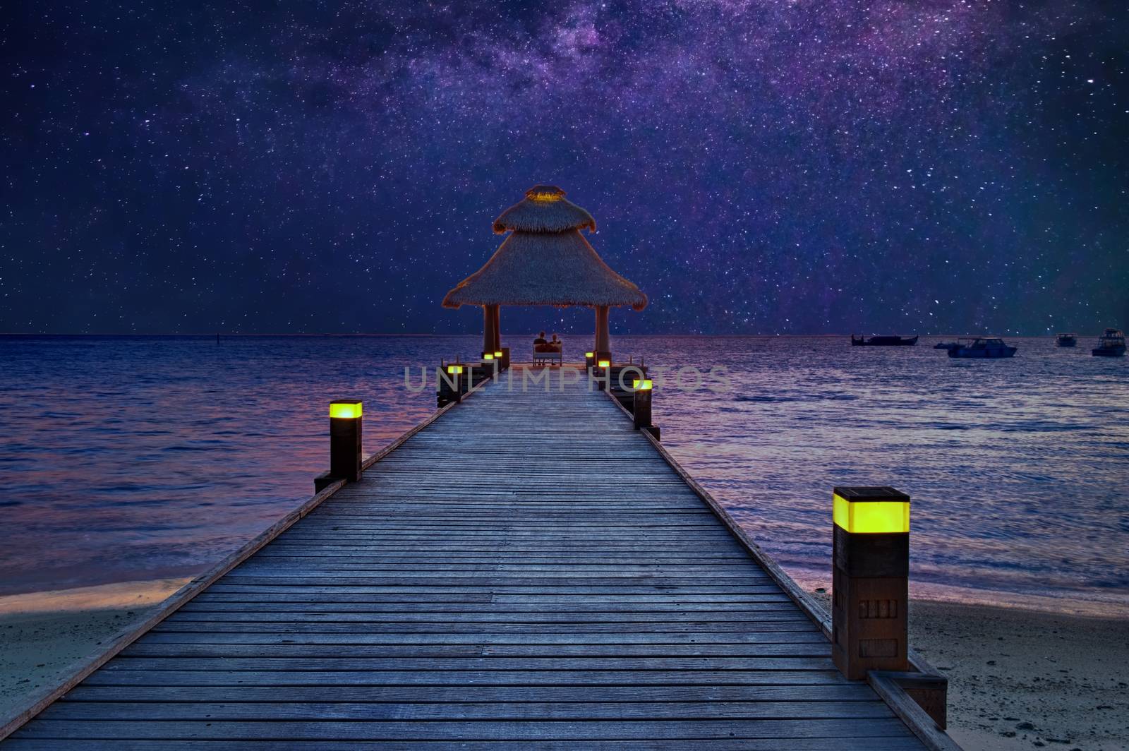 Romantic pair sitting on the jetty under the stars by the sea in the Maldives