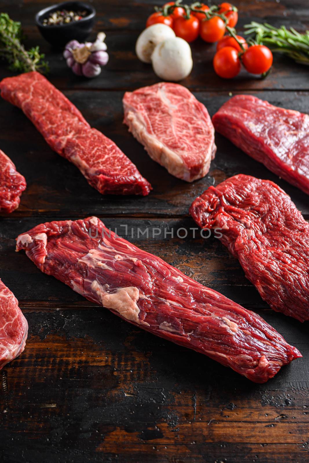 Alternative beef cut machete skirt steak close up in front of other cuts in butchery on old wood table side view selective focus vertical.