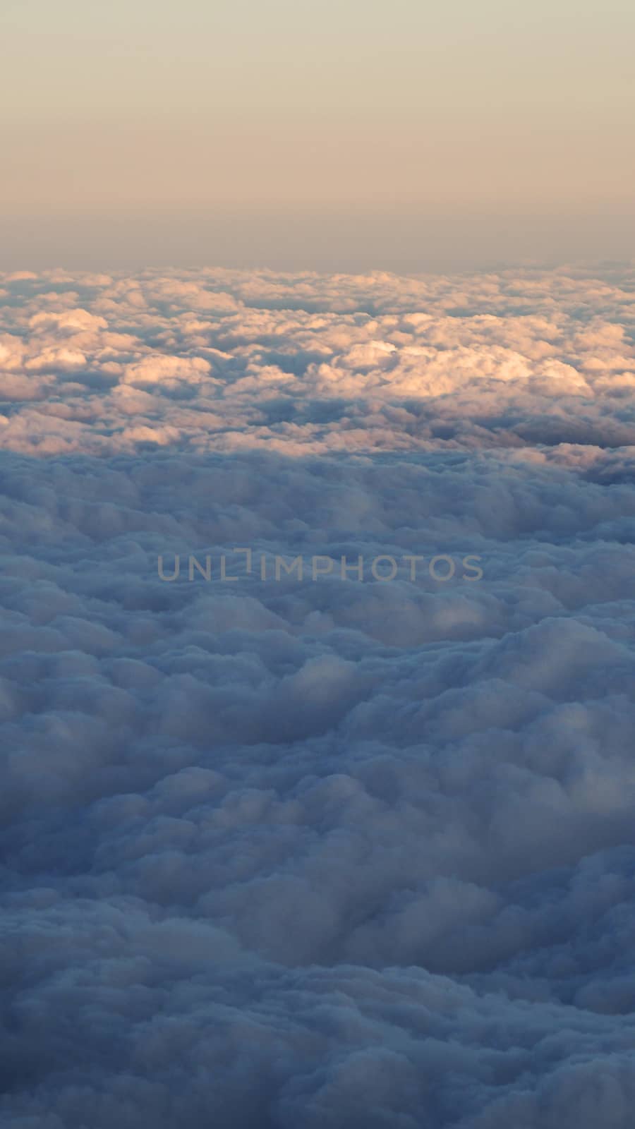 White clouds and blue sky with yellow warm sun light from airplane window.