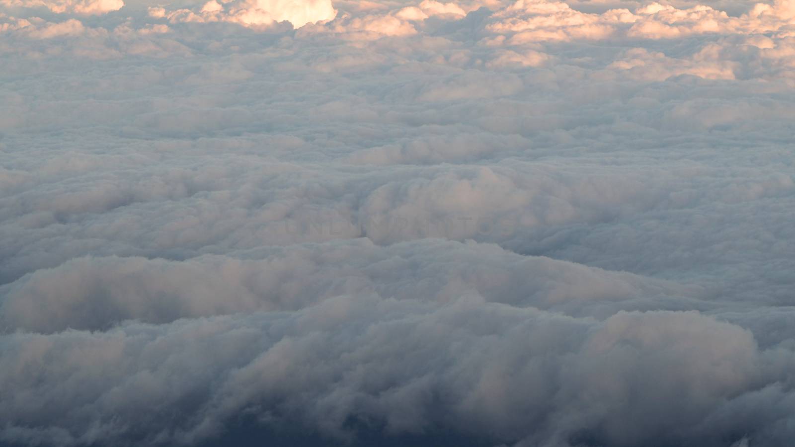 White clouds and blue sky with yellow warm sun light from airplane window.