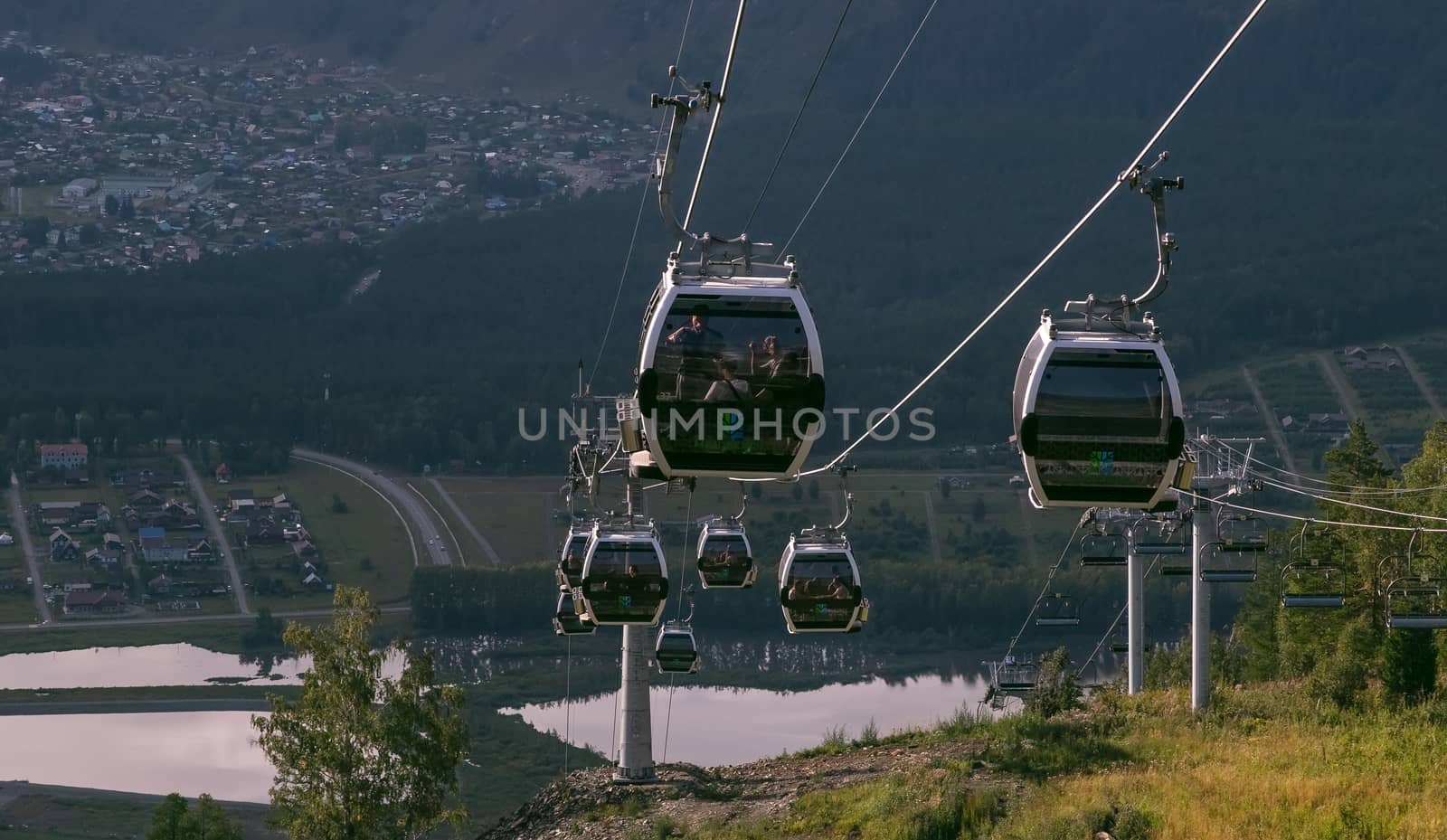Manzherok resort, Altai Mountains, Russia - August 12, 2020: High angle shot of cableway with tourists inside cable cars on a cityscape and landscape background