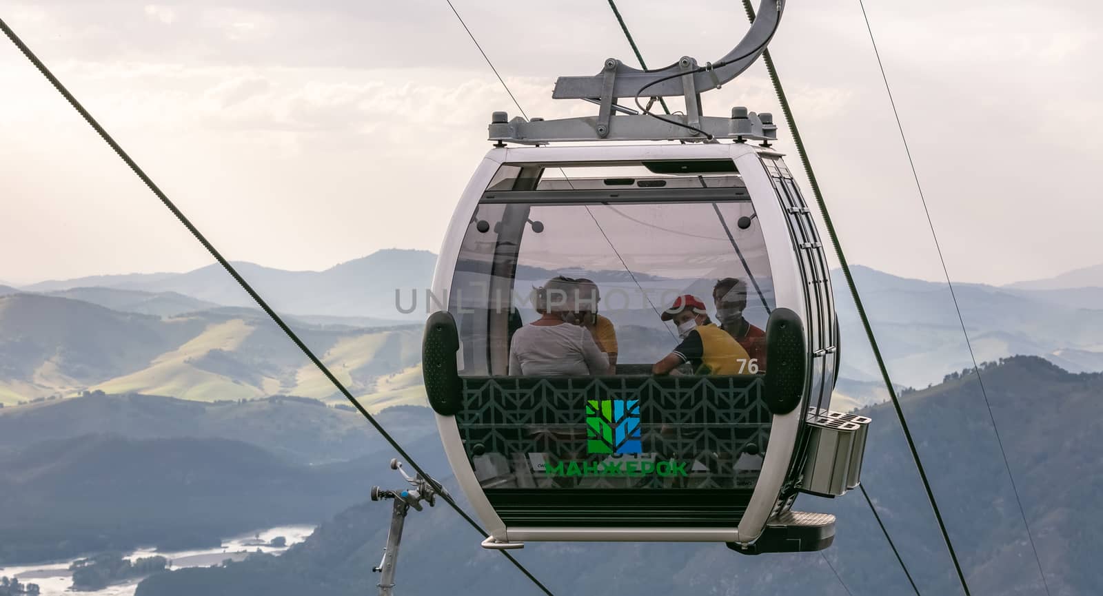 Manzherok resort, Altai Mountains, Russia - August 12, 2020: Shot of cable car with tourists inside of it wearing masks. Cloudy sky background. New Covid 19 reality concept.