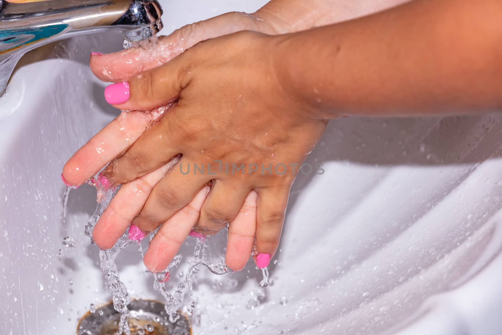 Close up shot of a woman washing her hands using tap water. Pink finger nails. Hygiene concept.