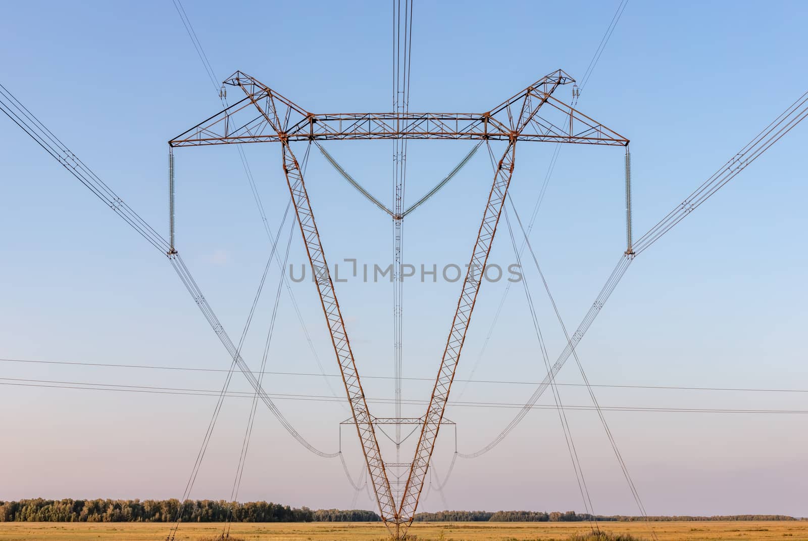 Low angle view of high voltage power lines and poles in the countryside. Blue sky as a background. Panoramic shot.