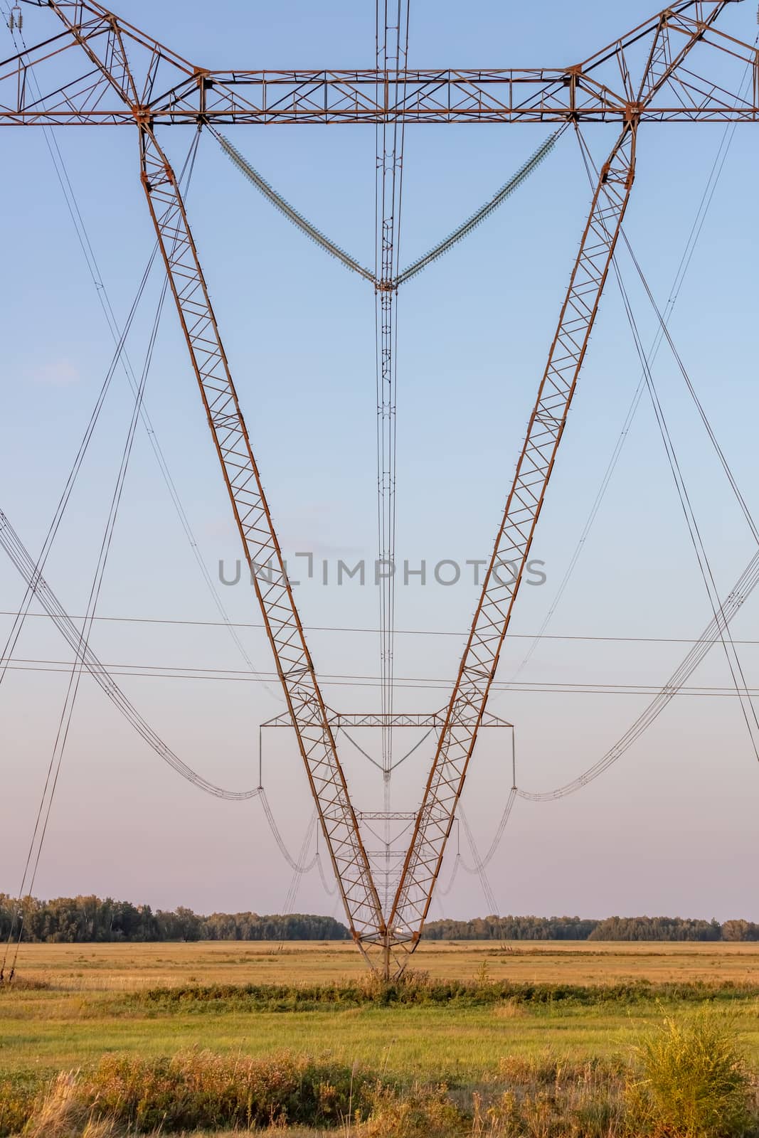 Low angle view of high voltage power lines and poles in the countryside. Blue sky as a background. Portrait format.