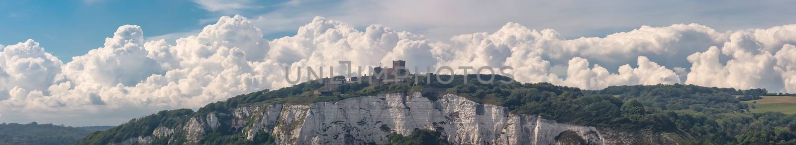 Wide angle panoramic shot of the White Cliffs of Dover, a castle on top of the cliff. Beautiful fluffy clouds and blue sky in the background.