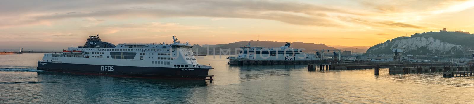 Port of Dover, England - June 24, 2020: Panoramic landscape shot of Dover Port with a P&O ferry boat docked and DFDS ferry boat docking at sunset. Beautiful warm orange sky and hills in the background