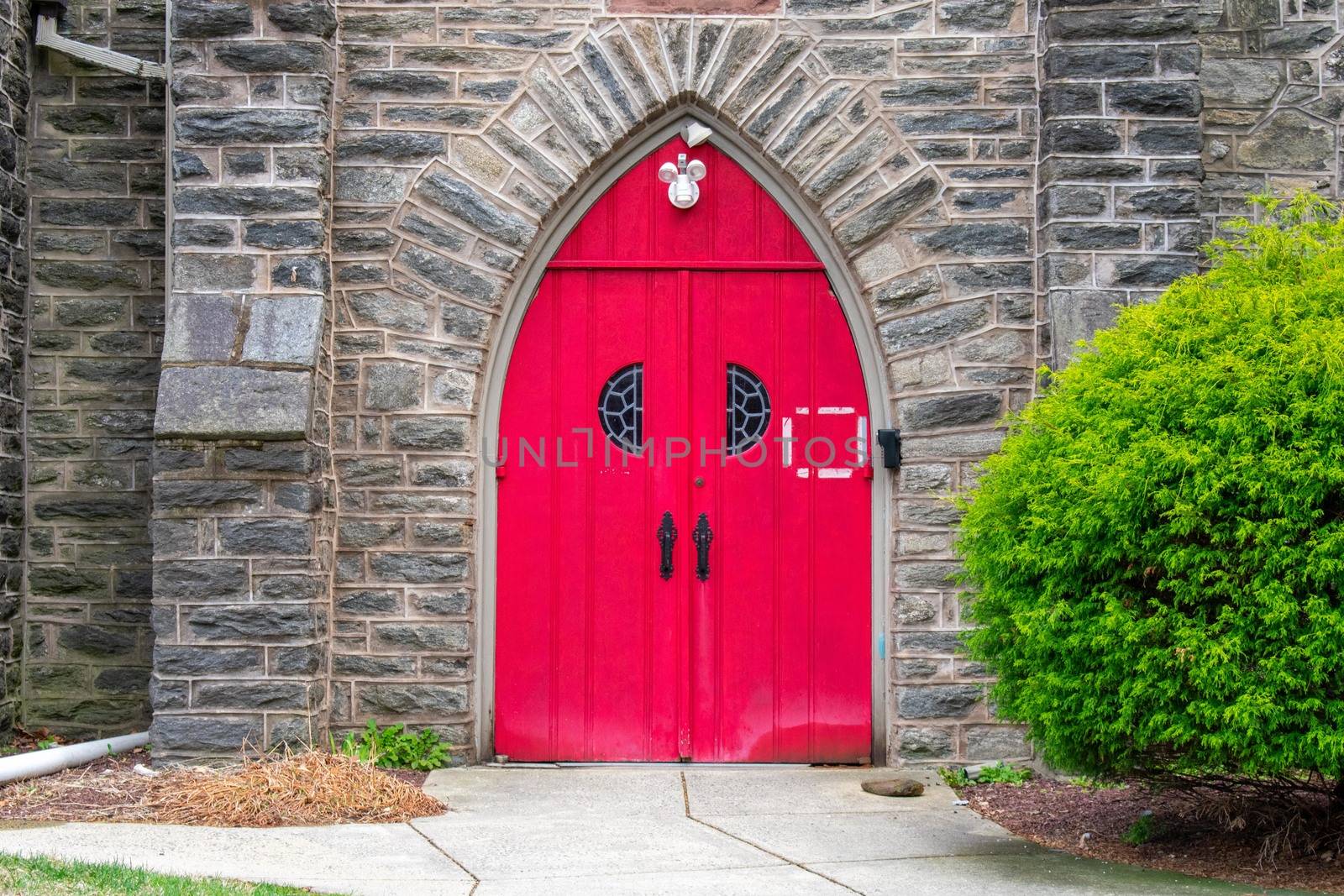 A Bright Red Door in a Cobblestone Church Wall With a Bush on the Side